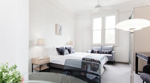 a white bedroom with a bed and a glass table at Excelsior Apartments at Glebe in Sydney