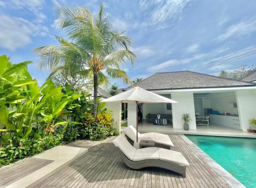einen Pool mit zwei Stühlen und einem Sonnenschirm neben einem Haus in der Unterkunft Alami Luxury Villa in Seminyak