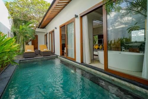 a swimming pool in front of a house with a bath tub at Anari Villas Kuta in Legian