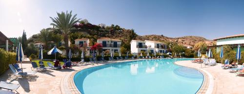 a large swimming pool with chairs and palm trees at Hylatio Tourist Village in Pissouri