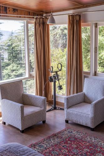 a living room with two chairs and large windows at Seclude Shimla, Taraview in Shimla