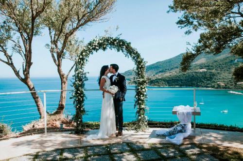 una sposa e uno sposo che si baciano sotto un arco al loro matrimonio di Artina Luxury Villa a Keríon