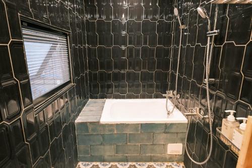 a black tiled bathroom with a tub and a window at South Gate Home Stay in Tainan