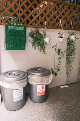 two trash cans sitting next to a wall with potted plants at South Gate Home Stay in Tainan