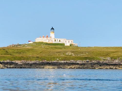 a lighthouse sitting on top of a hill next to the water at Carters Rest Guesthouse in Milovaig