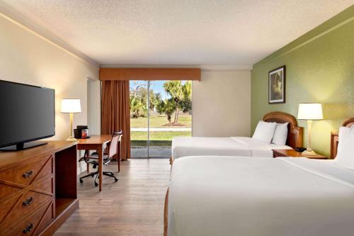 a hotel room with two beds and a desk and a television at Baymont by Wyndham Daytona Beach - Intl Speedway in Daytona Beach