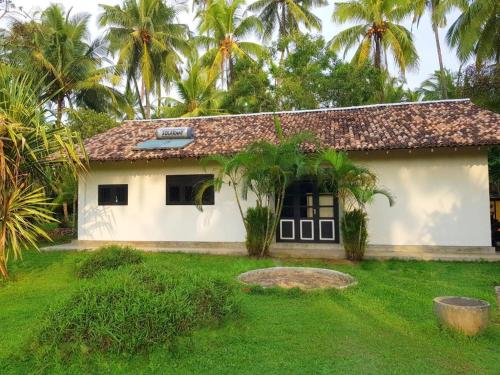 a small white house with palm trees in the background at Coconut Garden River Villa in Galle