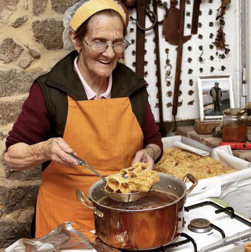 a woman in an apron stirring a pot of food at Le Corti Sarde Apartments in Bari Sardo