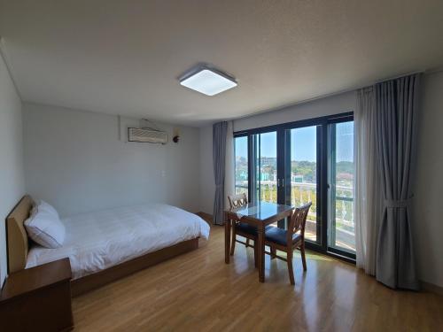 a bedroom with a bed and a table and a window at Hera Castle Pension in Seogwipo