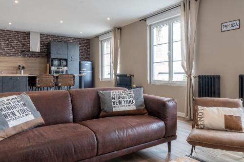 a living room with a brown couch and a kitchen at voyageurs in Valognes