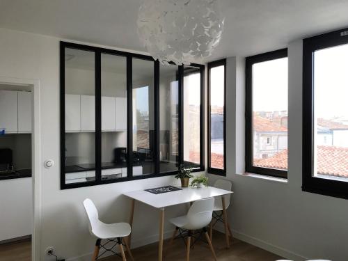 une salle à manger avec une table, des chaises et des fenêtres dans l'établissement Appartement Saint-Nicolas, à La Rochelle