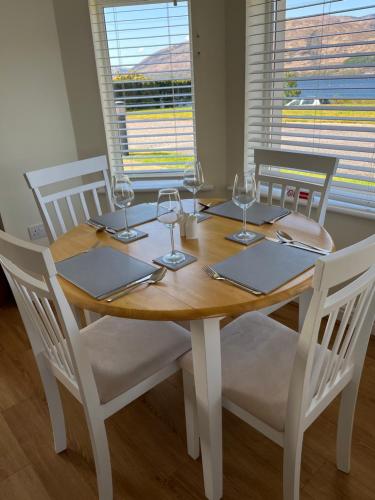 a wooden table with four chairs and wine glasses at Corran, Glenloch View, Fort William 2-Bedroom Loch Side Flat in Fort William