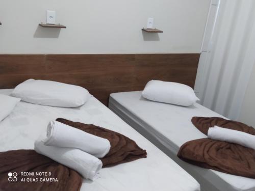 two beds in a room with white sheets and pillows at Pousada Quarto com ventilador,ar frigobar e garagem in Aparecida