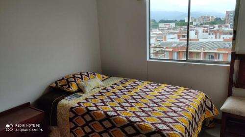 een slaapkamer met een bed met een kleurrijk dekbed en een raam bij Habitación en apartamento con ubicación estratética mejor sector sur in Cali