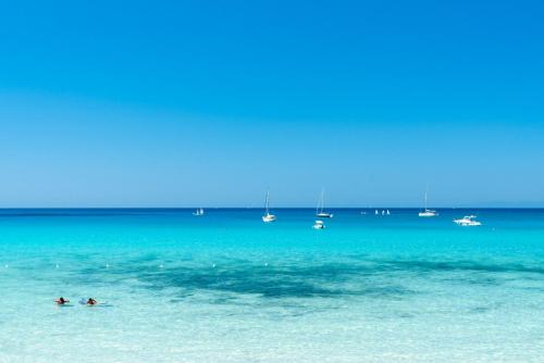 two people swimming in the ocean with boats in the water at Hotel Stella Maris in Villasimius