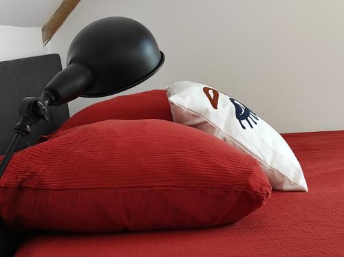 a red and white pillow on a bed with a lamp at Gites les Pourquoi Pas - Résidence de Tourisme DSV Bayeux in Bayeux