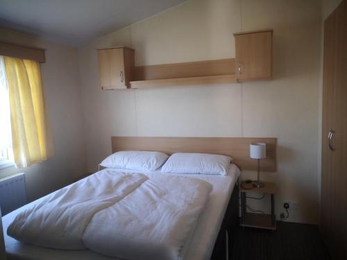 a bedroom with a bed with white sheets and a window at Caravan L25 in Mablethorpe