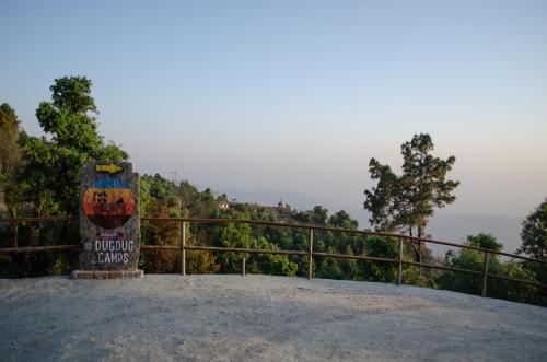 un cartello in cima a una collina con alberi sullo sfondo di DugDug Camps - Glamping Amidst Nature a Bhimtal