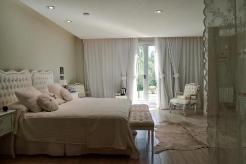 a white bedroom with a bed and a chair at La Posada Multiespacios in Dique Luján