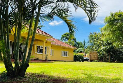 a yellow house with a palm tree in front of it at Buutu Nest in Jinja