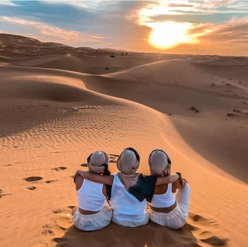 three people sitting in the desert watching the sunset at Sunset luxury camp in Hassilabied