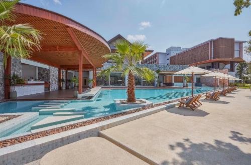 a swimming pool with chairs and palm trees next to a building at Laguna Grand Hotel & Spa Songkhla in Songkhla