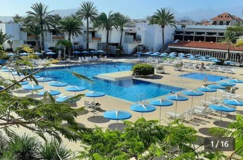 a large swimming pool with blue umbrellas and chairs at Ideal holiday apartment in the south of Tenerife in Costa Del Silencio