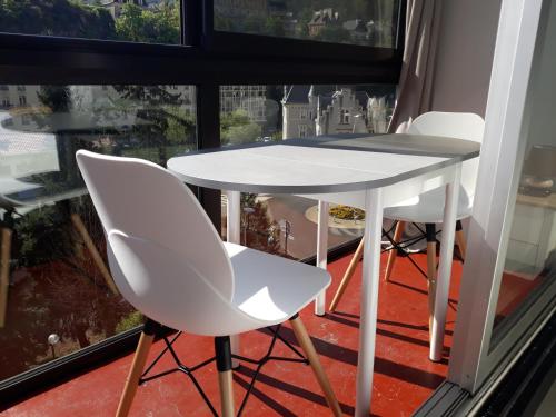 une table et des chaises blanches devant une fenêtre dans l'établissement Royat 64, à Royat