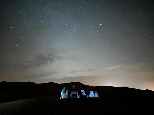 a group of three people sitting in the desert at night at Merzouga Paradise Luxury Camp in Merzouga