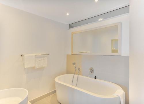 a white bathroom with a tub and a mirror at First floor with beautiful sea view in Cape Town