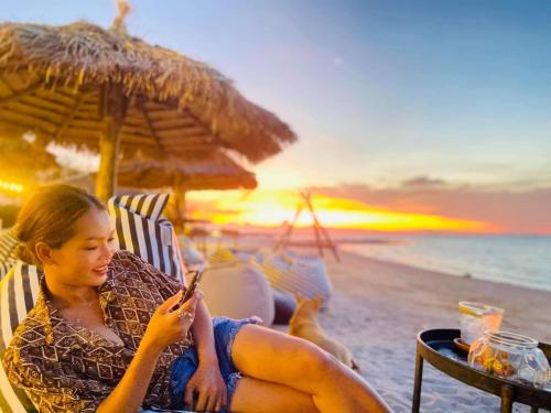 una mujer sentada en una silla en la playa mirando su celular en Sabai Sabai Beach Bungalows en Ko Phayam
