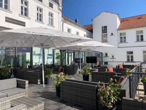 a patio with couches and umbrellas and tables at Parkhotel Putbus Superior International in Putbus