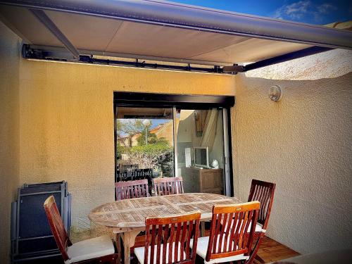 - une table et des chaises sur une terrasse avec une table et une fenêtre dans l'établissement Appartement mezzanine/jardin/terrasse village naturiste, au Cap d'Agde
