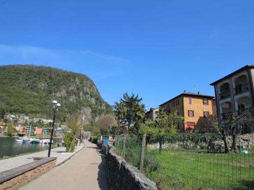 a street next to a river with buildings and a mountain at Apartment Lungolago by Interhome in Lavena Ponte Tresa