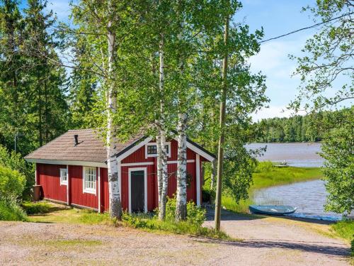 a red cabin with a boat in front of a lake at Holiday Home Peukaloinen by Interhome in Hirsjärvi