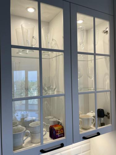 a cabinet filled with wine glasses and cups at PINEA Apartments Pobierowo z niesamowitym widokiem na morze oraz jacuzzi w wybranych apartamentach in Pobierowo