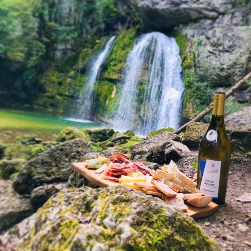 a bottle of wine and a plate of food next to a waterfall at Les balcons de Cuttura 2 & SPA chez Ô JurassiK in Cuttura