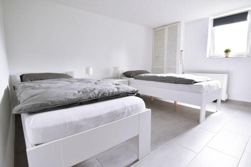 a white bedroom with two beds and a window at Souterrain apartment in Wesseling in Wesseling