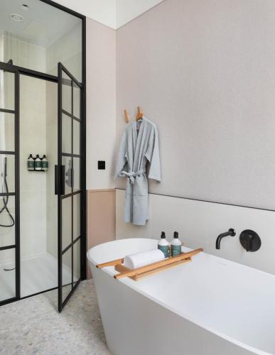 a bathroom with a bath tub and a robe on a wall at Inhabit Queen's Gardens, a Member of Design Hotels in London