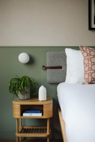 a bedroom with a bed and a nightstand with a plant at Inhabit Queen's Gardens, a Member of Design Hotels in London