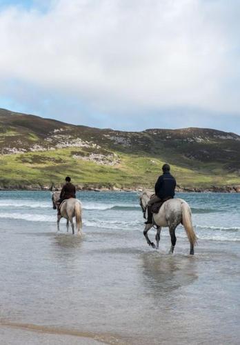 two people are riding horses on the beach at Kill House, Kingstown in Clifden