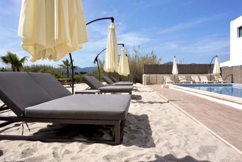 
a beach area with a couch, chair, and umbrella at Los Escondidos Ibiza in Playa d'en Bossa
