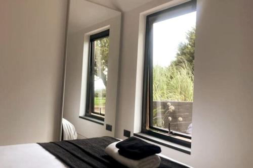 a bedroom with two windows and a bed with a view at The Cabin at Barnstormers, luxury woodland setting in Marldon