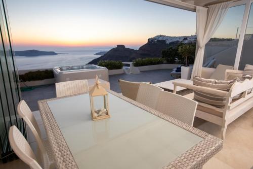 Sunset View Villa Santorini - with Outdoor Jacuzzi في فِروستيفاني: طاولة وكراسي على شرفة مطلة على المحيط