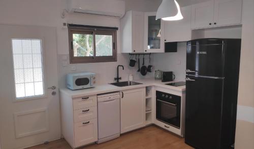 una cucina con armadietti bianchi e frigorifero nero di אחת ויחידה - One & Only a Ma'alot Tarshiha