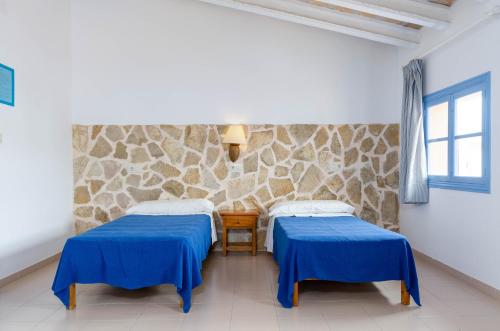 two beds in a room with a stone wall at Hostal Marina in Cala Ratjada