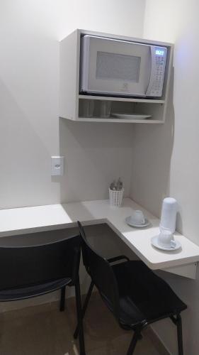 eine Mikrowelle über einem weißen Schreibtisch mit einem schwarzen Stuhl in der Unterkunft Pousada Quarto Casal com ar,frigobar, garagem in Aparecida