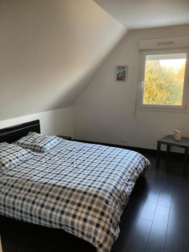 a bedroom with a bed with a plaid blanket and a window at A proximité des plages Normandes in Cairon
