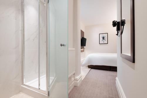 a bathroom with a glass shower and a bed at Rove Hotel London Paddington in London