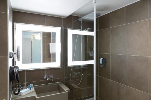 ein Badezimmer mit zwei Spiegeln, einem Waschbecken und einer Dusche in der Unterkunft Novotel Berlin Mitte in Berlin